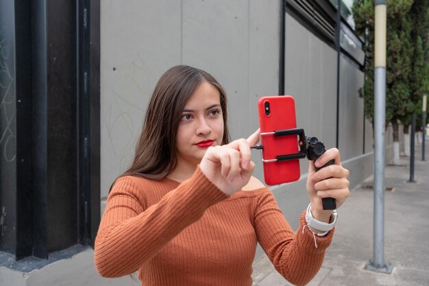 Jonge vrouw die videovlog maakt met smartphone en gimbal-stabilisator buiten, vloggen op straat