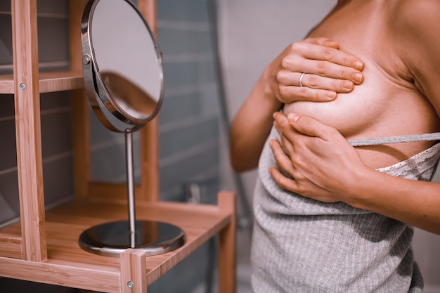 Jonge vrouw die voor de spiegel staat en haar borst controleert terwijl ze zelfonderzoek doet. Borstkanker bewustzijn. Hoe controleer ik het borstconcept.