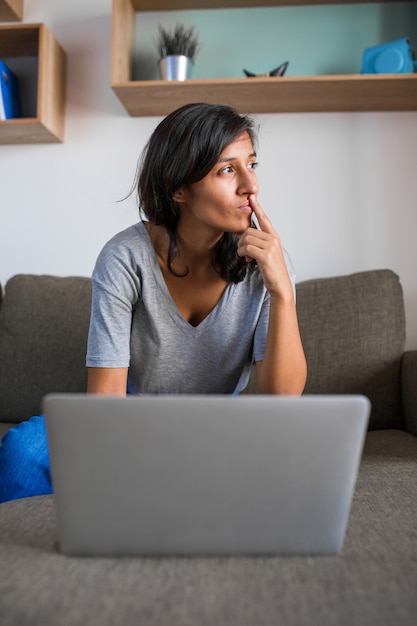 Jonge vrouw die voor een computer thuis denkt