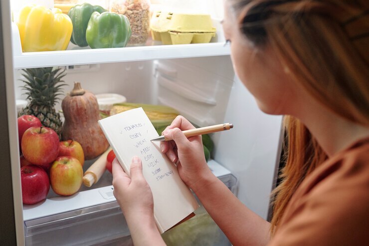 Foto jonge vrouw die voor een geopende koelkast staat en controleert of ze alles van het boodschappenlijstje heeft gekocht
