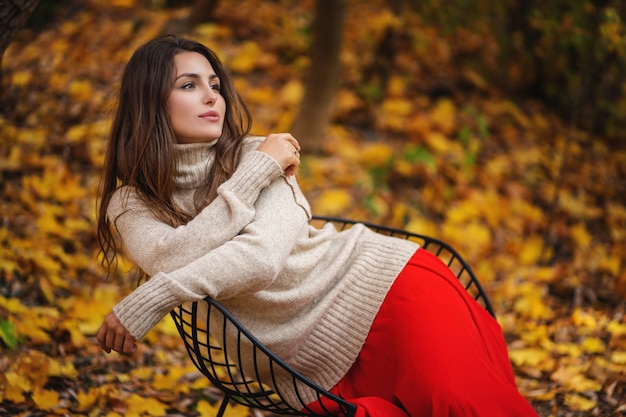 Jonge vrouw die warme sweater op een gang in het park draagt bij zonnige de herfstdag