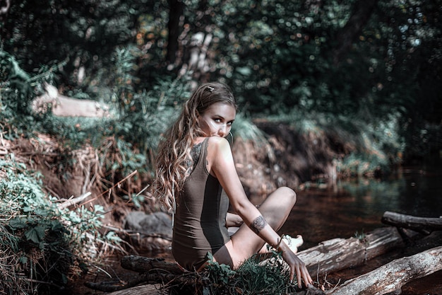 Foto jonge vrouw die wegkijkt terwijl ze op hout zit in het bos