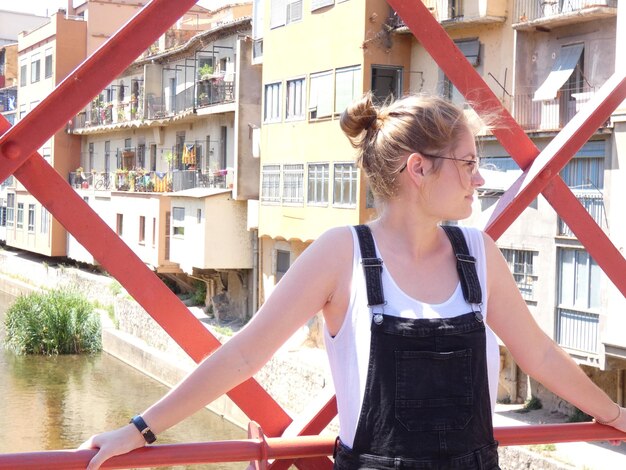 Foto jonge vrouw die wegkijkt terwijl ze tegen gebouwen in de stad staat