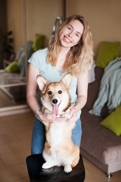 Jonge vrouw die Welse corgipuppy dichtbij haar gezicht houdt. Welsh Corgi Pembroke-puppy, vrolijke snit