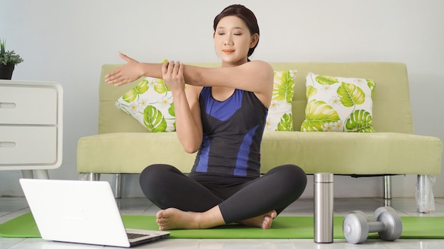 Jonge vrouw die yoga beoefent en bewegingen imiteert vanaf haar laptopscherm