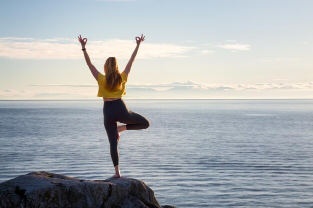 Jonge vrouw die yoga beoefent op een rotsachtig eiland tijdens een levendige zonsondergang