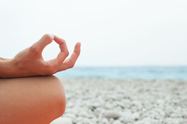 Jonge vrouw die yoga beoefent op het strand close-up van handen gyan mudra en lotuspositie