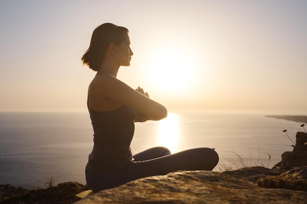 Jonge vrouw die yoga beoefent over zonsondergang zee