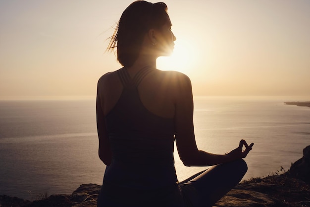 Jonge vrouw die yoga beoefent over zonsondergang zee