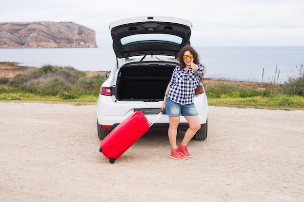 Jonge vrouw die zich dichtbij achterkant van auto bevindt die en zich klaar maakt om te gaan glimlachen. zomer roadtrip