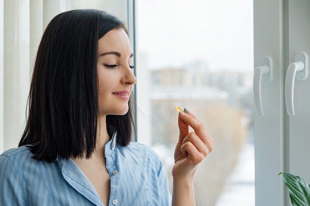 Jonge vrouw die zich dichtbij het venster bevindt dat vitamine neemt