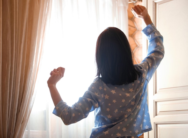 Jonge vrouw die zich uitstrekt in de buurt van raam in slaapkamer Luie ochtend