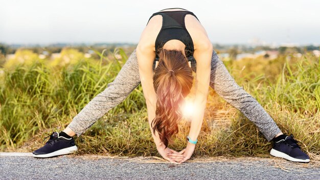 Foto jonge vrouw die zich uitstrekt terwijl ze op de weg tegen de lucht staat