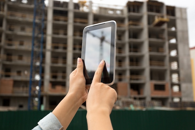 Jonge vrouw die zich voordeed op de bouwplaats en digitale tablet gebruikt