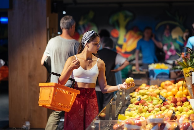 Jonge vrouw doet boodschappen in de supermarkt en kiest appels in de winkel