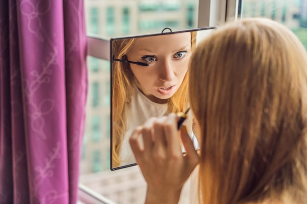 Foto jonge vrouw doet make-up bij het raam met een panoramisch uitzicht op de wolkenkrabbers en de grote