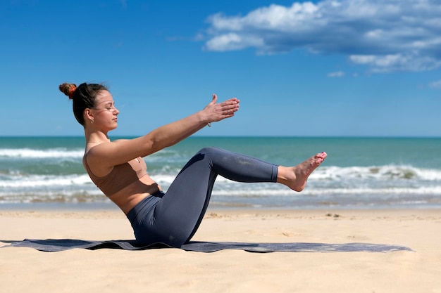 Jonge vrouw doet pilates aan de kust van het strand in sportkleding