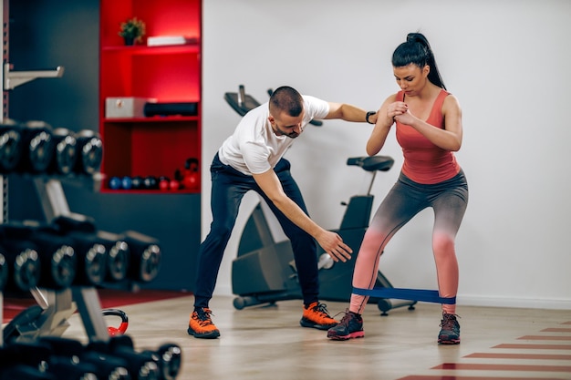 Jonge vrouw doet training voor benen met personal trainer in de sportschool.