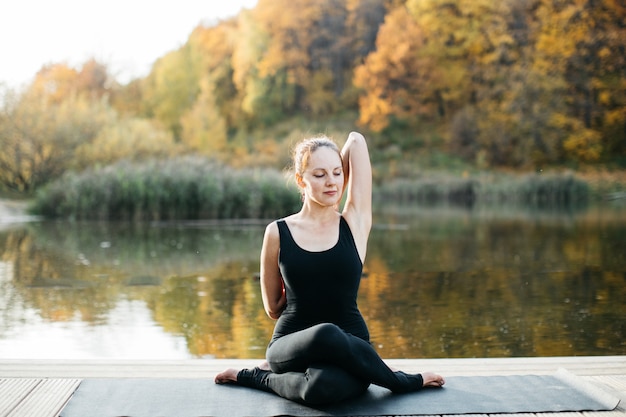 Jonge vrouw doet yoga asana in de natuur in de buurt van het meer