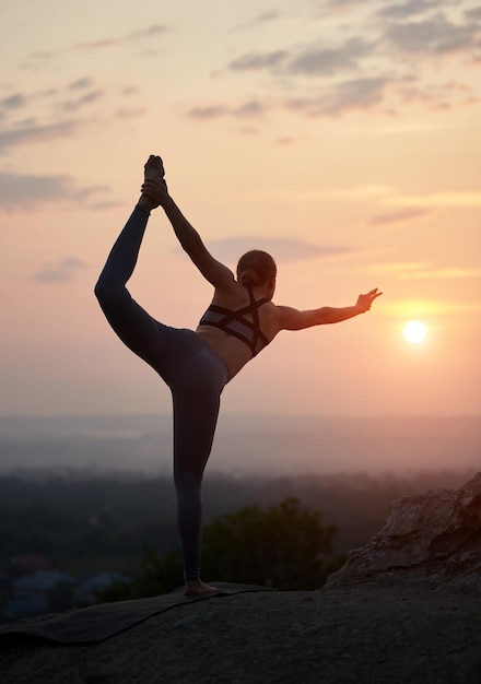 Jonge vrouw doet yoga-oefeningen buiten bij zonsondergang