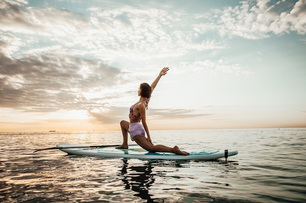 Foto jonge vrouw doet yoga op een sup-bord in het meer bij zonsopgang