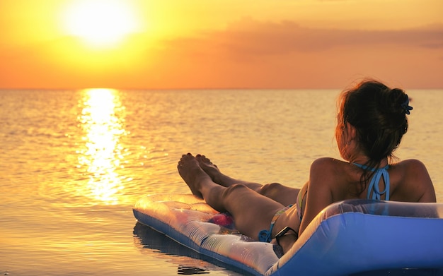 Jonge vrouw draagt bikini ligt op opblaasbare matras op zonsondergang oranje kleur achtergrond zomervakantie zee rust zon tan concept