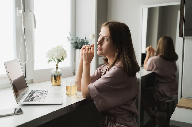 Jonge vrouw draagt slaapkleding die op laptop werkt terwijl ze in de woonkamer zit en thee drinkt sociaal netwerk en thuis werkt concept