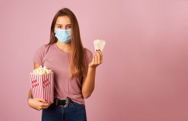 Jonge vrouw dragen masker met popcorn en bioscoopkaartjes