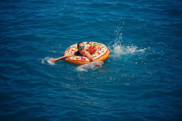 Jonge vrouw drijvend op een opblaasbare grote donut in de transparante turquoise zee Weergave van een slanke dame ontspannen op vakantie in Turkije Egypte Middellandse Zee