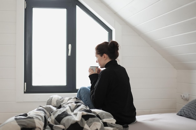 Jonge vrouw drinkt koffie en geniet thuis van een heerlijke ochtend in de lichte kamer