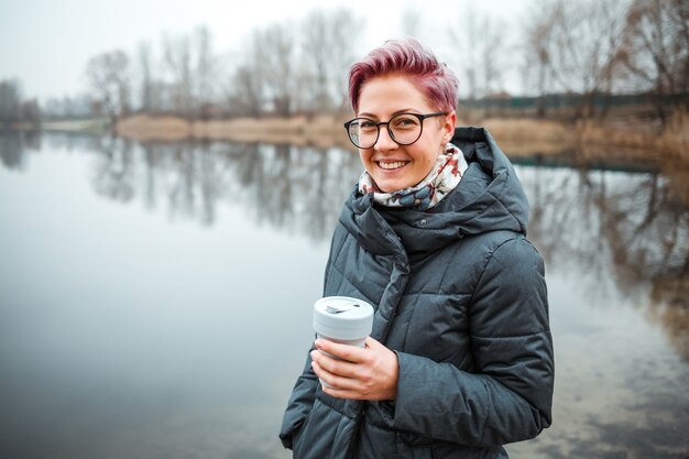 Jonge vrouw drinkt koffiekopje op de oever van het meer