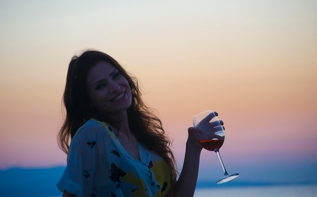 Jonge vrouw drinkt rode wijn bij zonsondergang