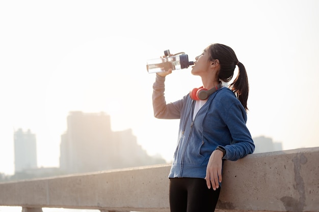 Jonge vrouw drinkt water en staat om te rusten na het joggen van een ochtendtraining in de stad. Een stad die gezond leeft in de hoofdstad. Oefening, fitness, joggen, hardlopen, levensstijl, gezond concept.