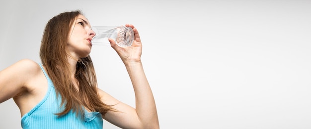 Jonge vrouw drinkwater uit een glas tegen een witte muur Banner