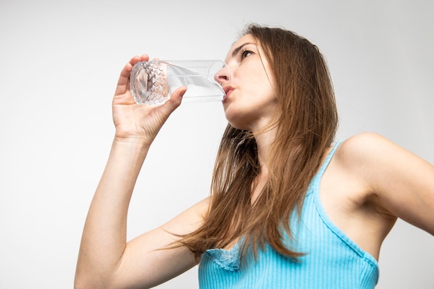 Jonge vrouw drinkwater uit een glas tegen een witte muur