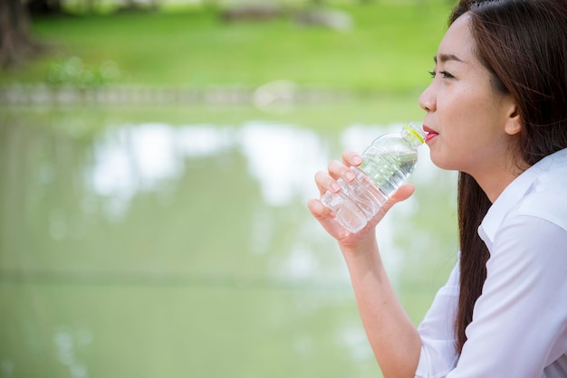 Jonge vrouw drinkwater uit fles in groene tuin Park Aziatische vrouwelijke drinkwater fles gezond persoon gelukkig en lachend Geluk mooie Aziatische chinese vrouwen houden fles mineraalwater