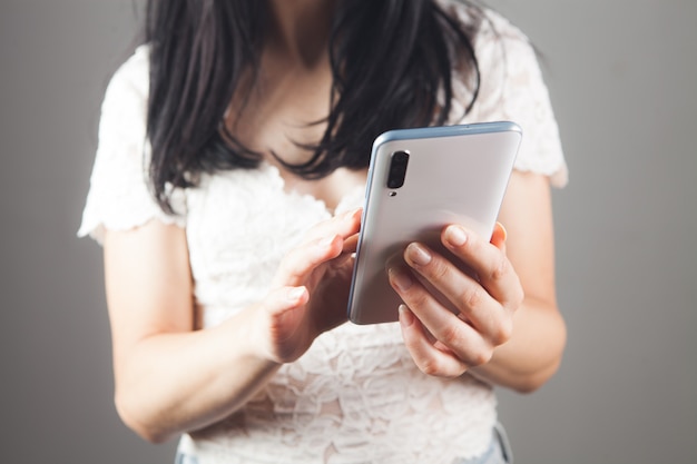 Jonge vrouw drukt op het telefoonscherm op een grijze achtergrond