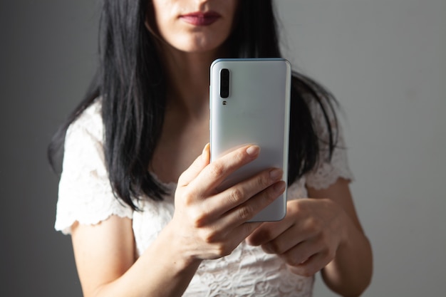 Jonge vrouw drukt op het telefoonscherm op een grijze achtergrond