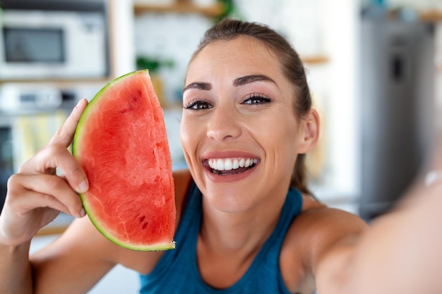 Jonge vrouw eet een plakje watermeloen in de keuken Portret van een jonge vrouw die geniet van een watermeloen