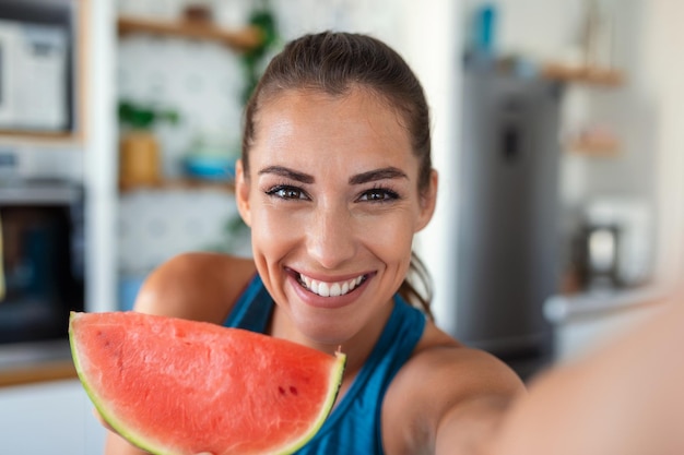 Jonge vrouw eet een plakje watermeloen in de keuken Portret van een jonge vrouw die geniet van een watermeloen