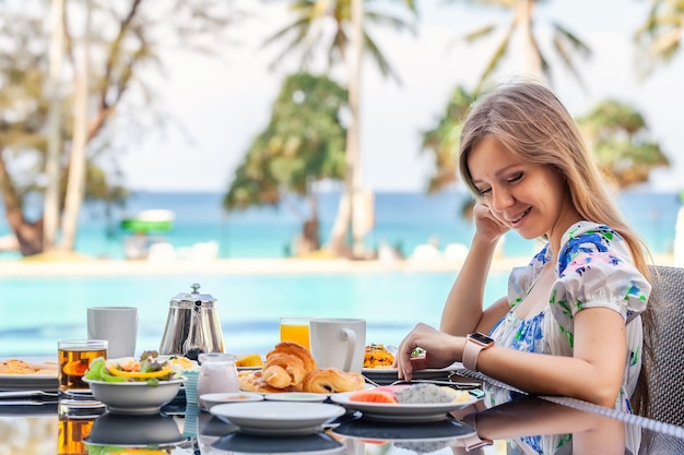 Jonge vrouw eet ontbijt in resort restaurant zwembad turquoise zee achtergrond