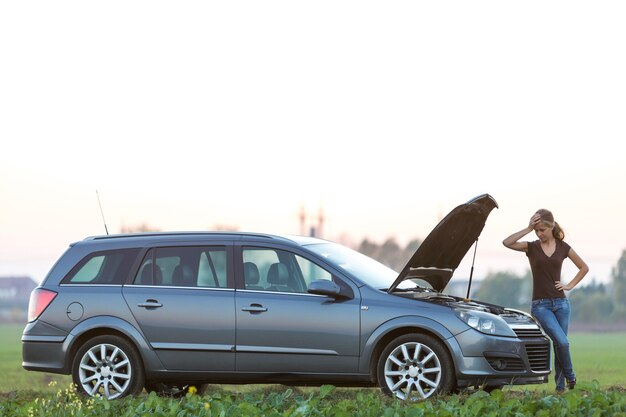 Jonge vrouw en een auto met geknalde kap. Transport, voertuigproblemen en storingen concept.