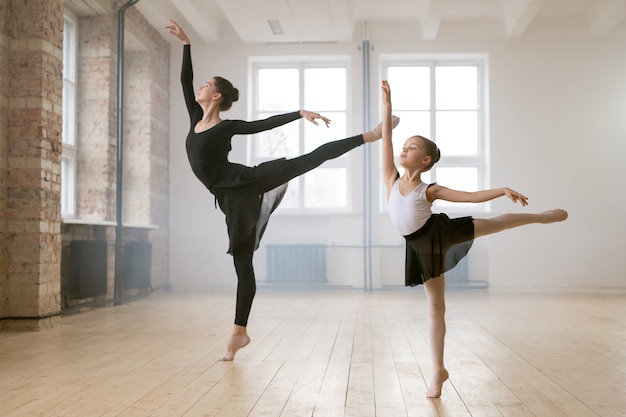 Jonge vrouw en klein meisje staan samen in dezelfde ballethouding en dansen in dansstudio