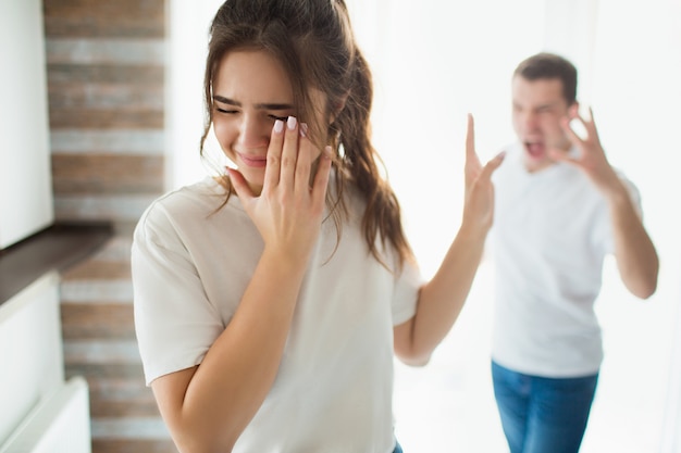 Jonge vrouw en man in de kamer. Guy misbruik meisje en schreeuw op haar. Vrouw lijden en huilen. Emotionele ziekte en psychologische druk.