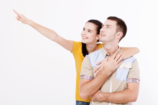 Jonge vrouw en man met witte perfecte glimlach in zomerkleding toont punten voor vingers opzij op lege ruimte over witte muur.