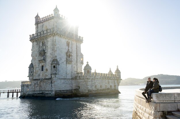 Jonge vrouw en man zitten naast de Belem-toren in Lissabon