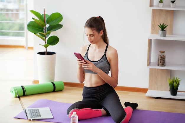 Jonge vrouw en thuis oefeningen doen op yogamat tegenover laptop