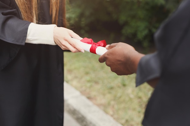 Jonge vrouw en zwarte man met diploma. Onderwijs, kwalificatie en toga concept.