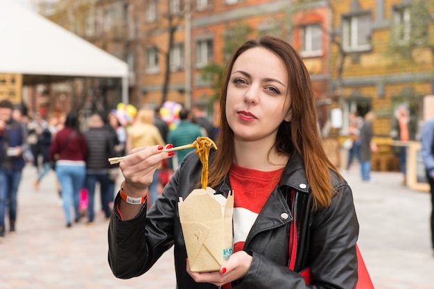 Jonge vrouw eten Aziatische afhaalmaaltijden op drukke festival