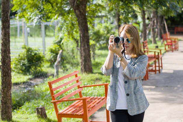 Foto jonge vrouw fotografeert met haar mobiele telefoon terwijl ze in het park staat